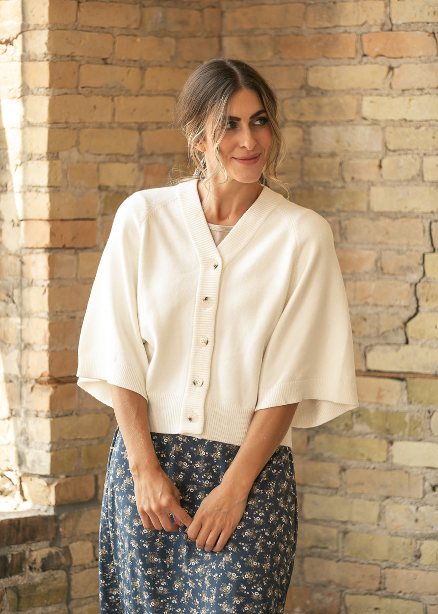 Cream V neck button down cardigan with wide sleeves and ribbed trim, styled with a navy floral skirt.