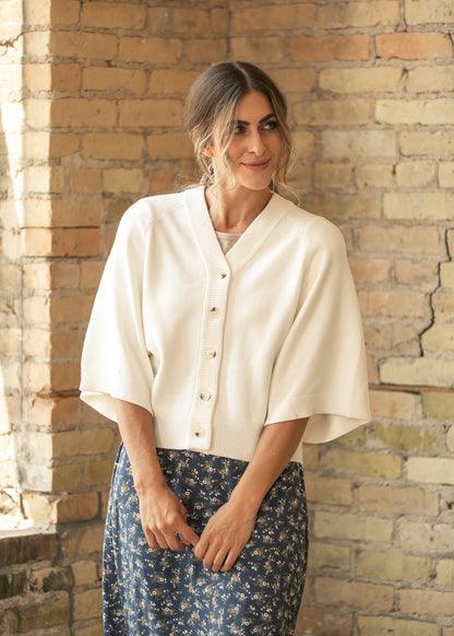 Cream V neck button down cardigan with wide sleeves and ribbed trim, styled with a navy floral skirt.