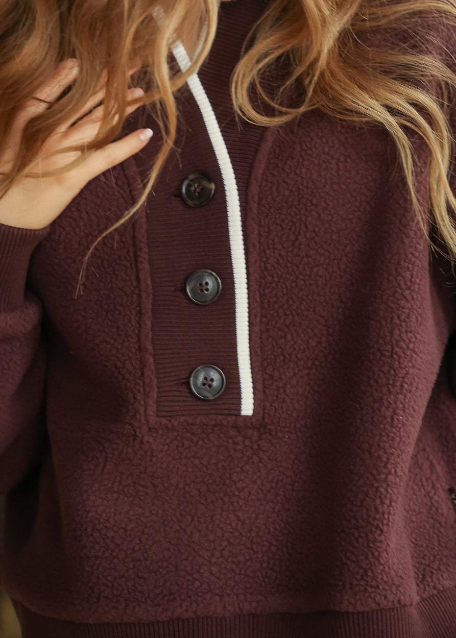 Close-up of Mahogany fleece pullover showing ribbed button neckline, contrast trim, and plush texture.