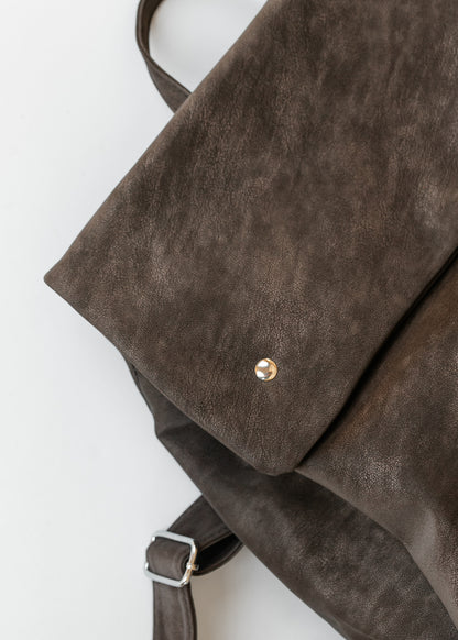 Close-up of chocolate brown backpack showing the vintage matte texture, metal snap detail, and adjustable strap buckle.