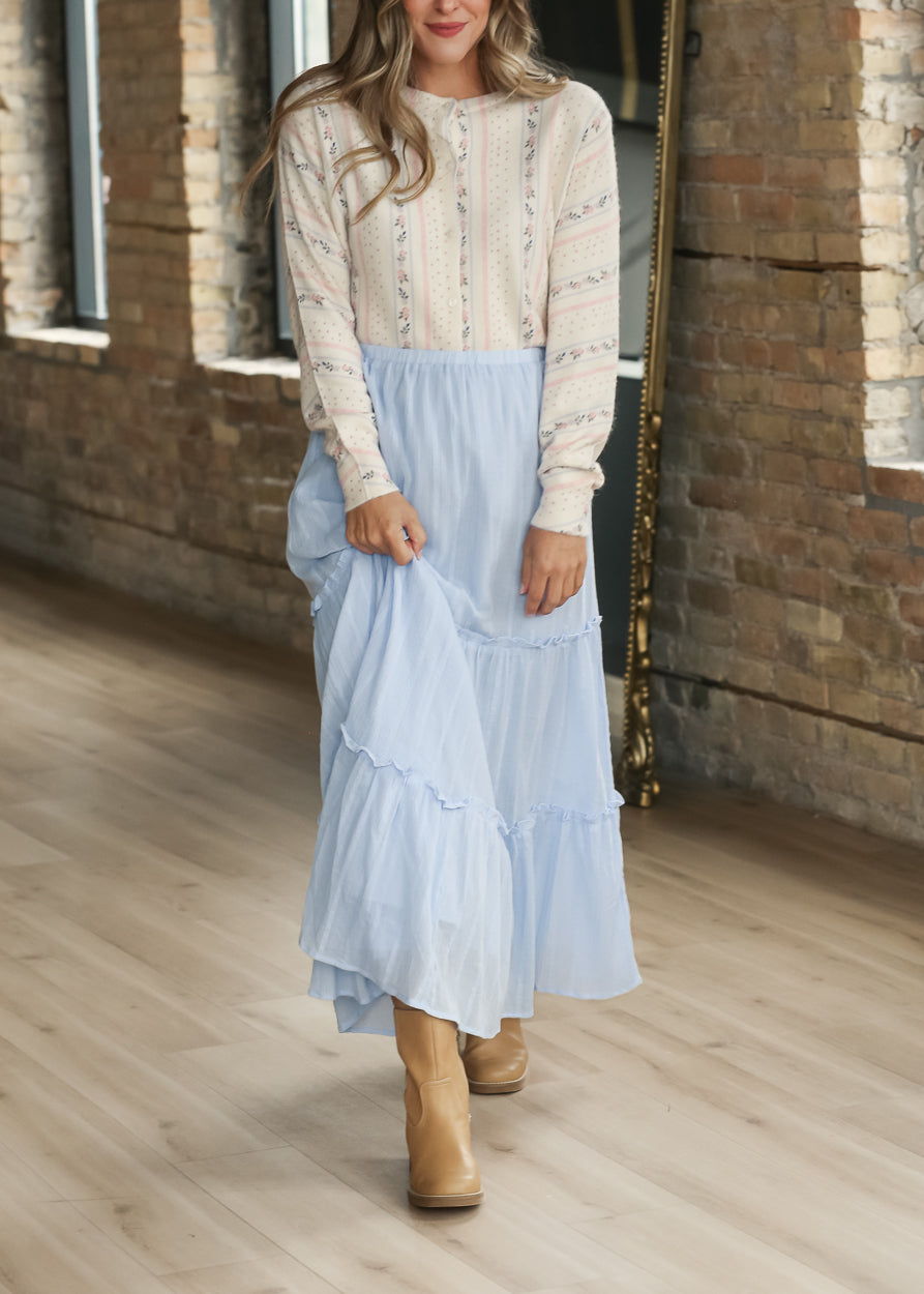 Cream button-front knit cardigan styled with a light blue maxi skirt and neutral boots.