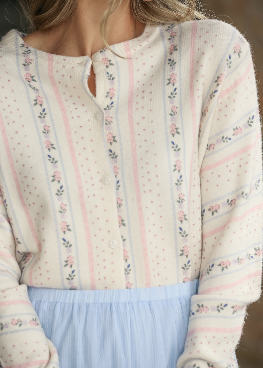 Close-up of cream knit cardigan showing pink and blue floral stripes and functional buttons.