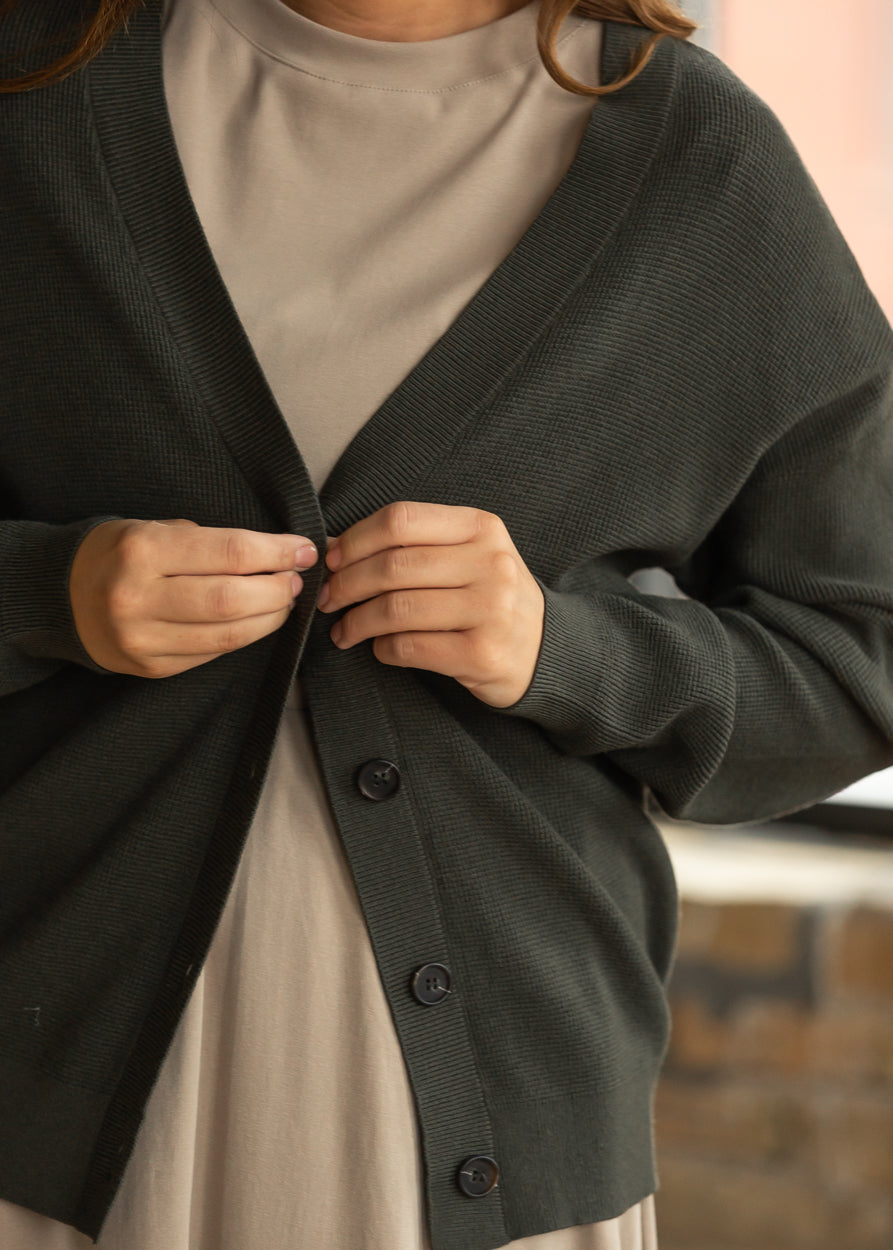 Dark olive knit cardigan styled open over a taupe midi dress