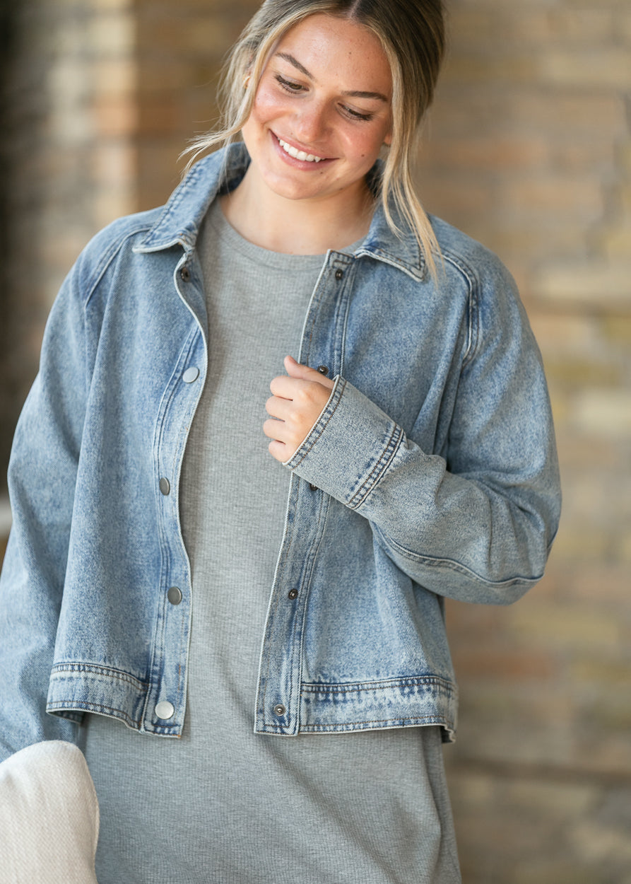 Close-up of light wash denim jacket showing snap closure, collar, and relaxed long sleeves.