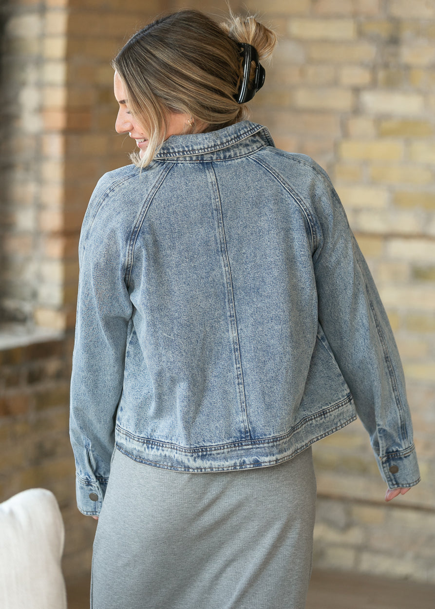 Back of light wash cropped denim jacket showing raglan-style seams and relaxed silhouette.