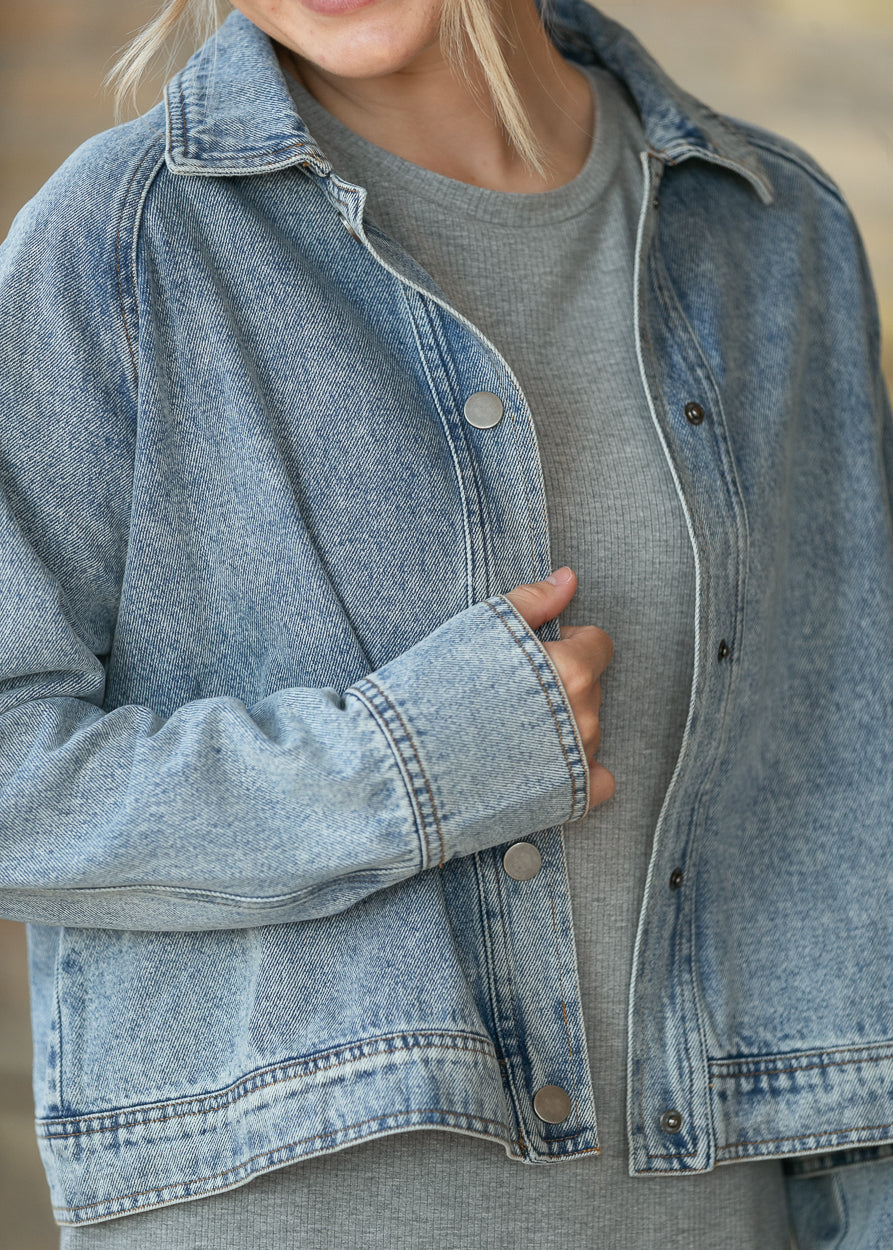 Close-up of washed denim jacket showing snap-front closure, cuff, collar, and denim texture.