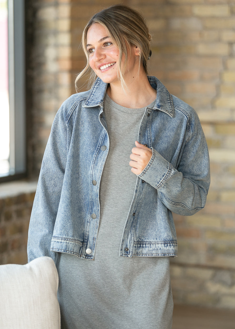 Light wash cropped denim jacket with snap front, classic collar, and relaxed fit styled over a gray dress.