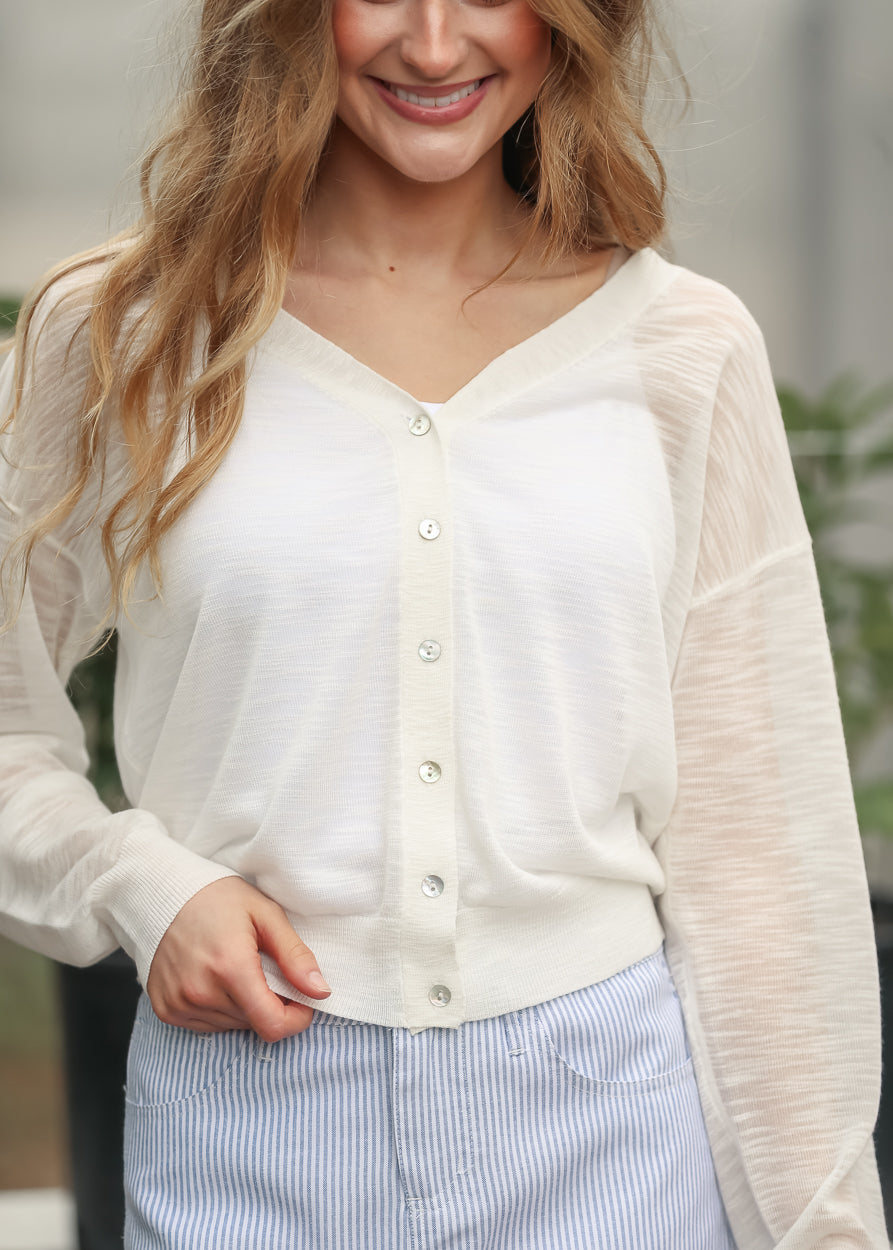 Close-up of white lightweight cardigan with functional buttons and sheer knit texture