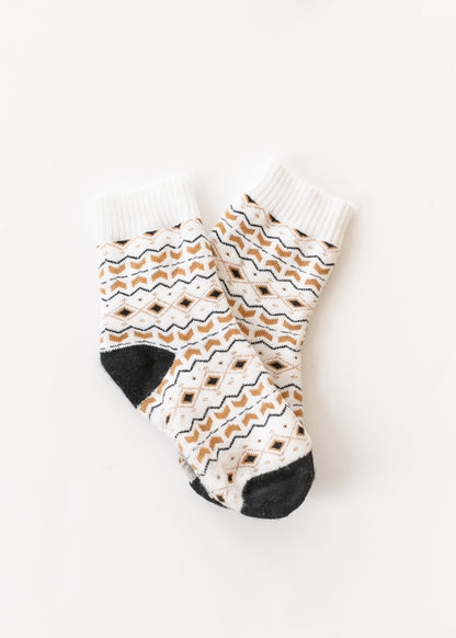 White Nordic Fair Isle knit crew socks with tan and black geometric pattern, ribbed cuffs, and contrasting black heels and toes.
