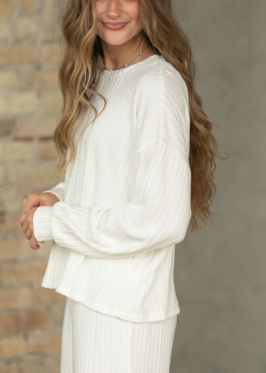 Side view of bone white ribbed long sleeve top showing loose fit, vertical texture, and gathered cuffs.
