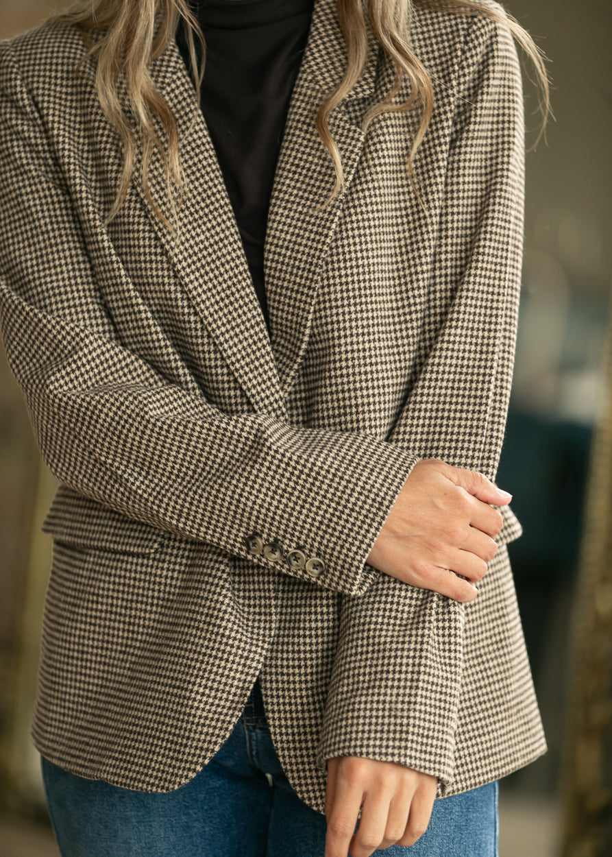Close-up of tan and black check blazer showing single-button front, notched lapel, and flap pocket.