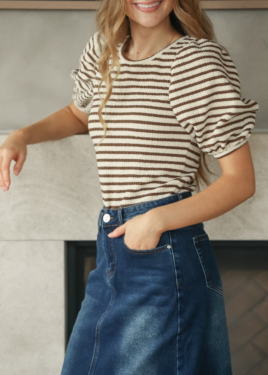 Side view of brown and cream striped tee styled with a dark wash denim maxi skirt.