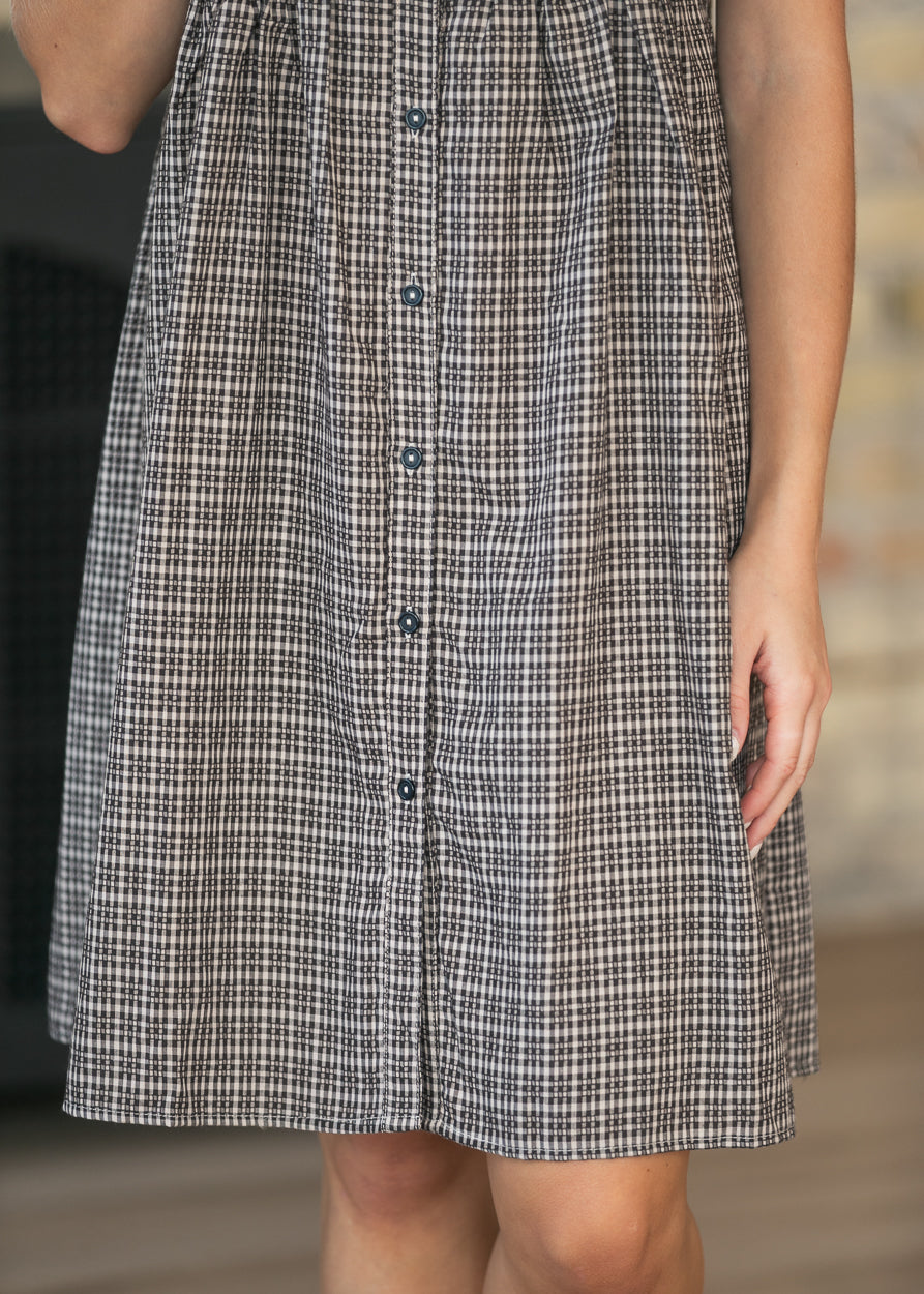 A close-up of a person wearing a sleeveless button-front dress with a small-scale black, white, and gray gingham pattern.