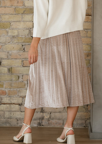 Back of tan pink velvet midi skirt showing allover pleats and a no-slit hem, styled with ivory block heels.