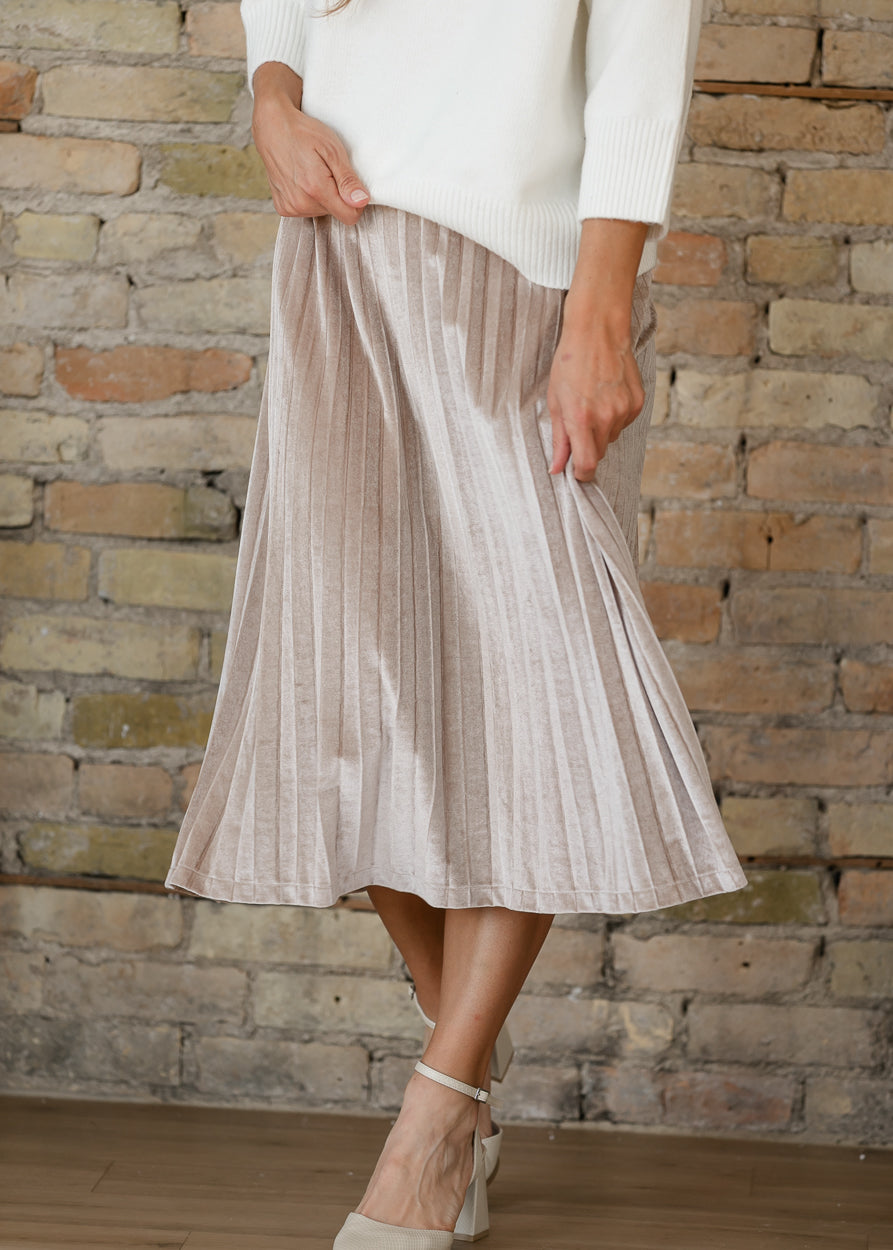 Regina tan pink velvet skirt with flowing pleats, shown with the fabric held out above ivory ankle-strap heels.