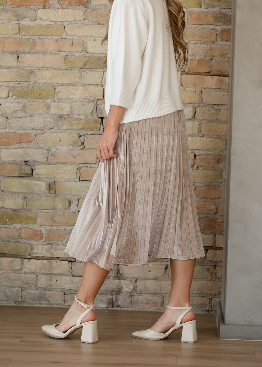 Side of Regina tan pink pleated midi skirt in motion, paired with an ivory sweater and ankle-strap heels.