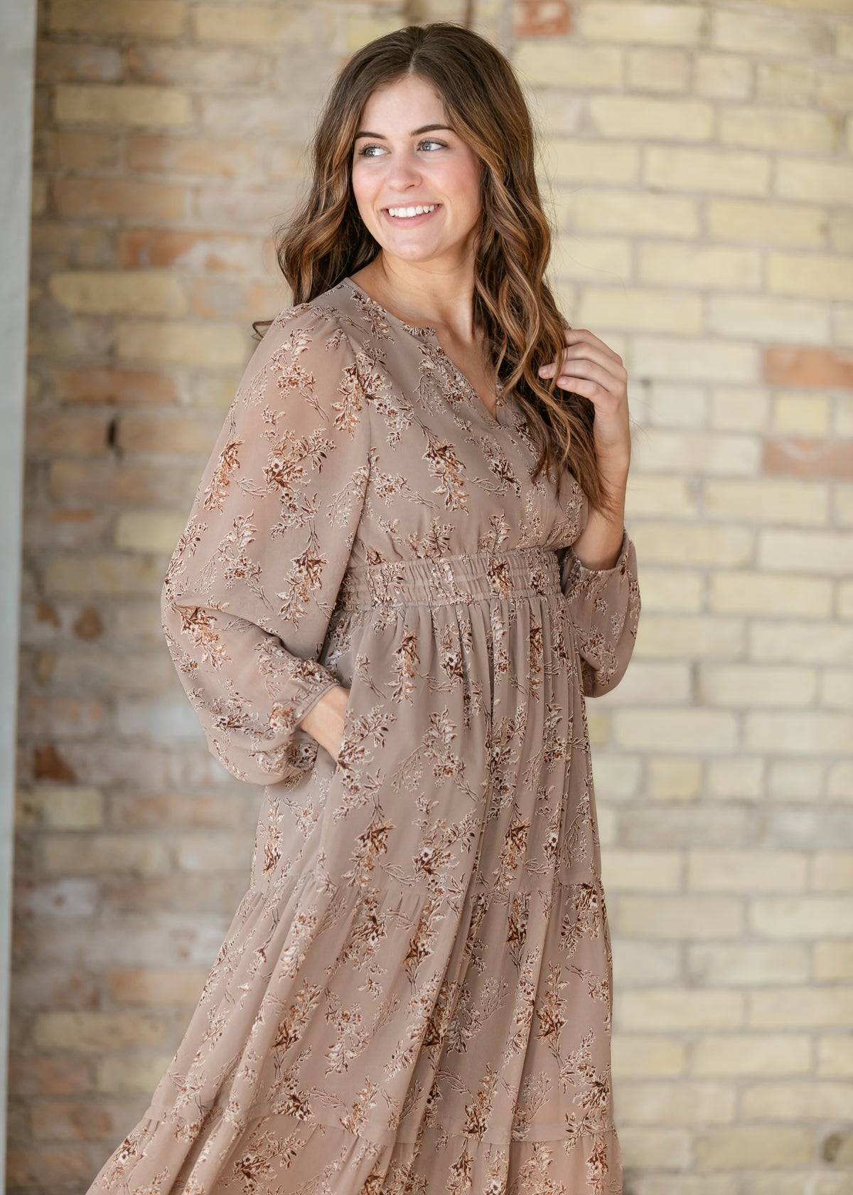 Brown floral maxi dress shown from an angled view with gathered waist and long sleeves.