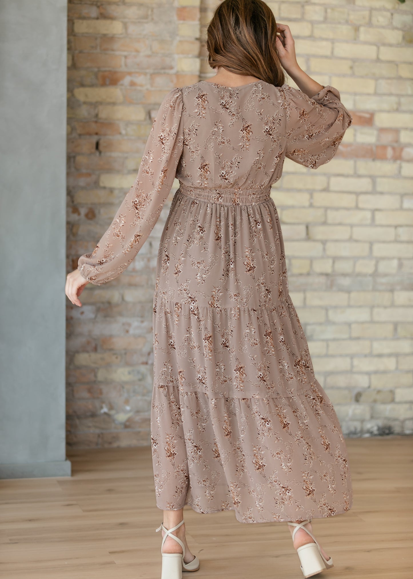 Back view of brown floral maxi dress showing the long sleeves, gathered waist, and tiered skirt.