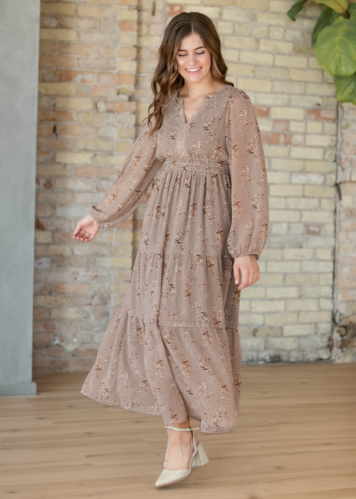 Brown floral maxi dress with long sleeves and tiered ankle-length skirt styled with neutral heels.