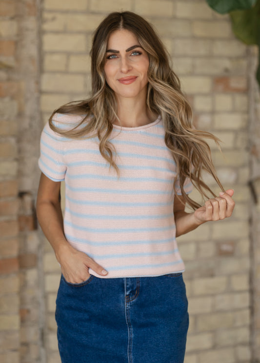 Pastel pink and blue striped sweater worn with a denim skirt, model holding the hem.