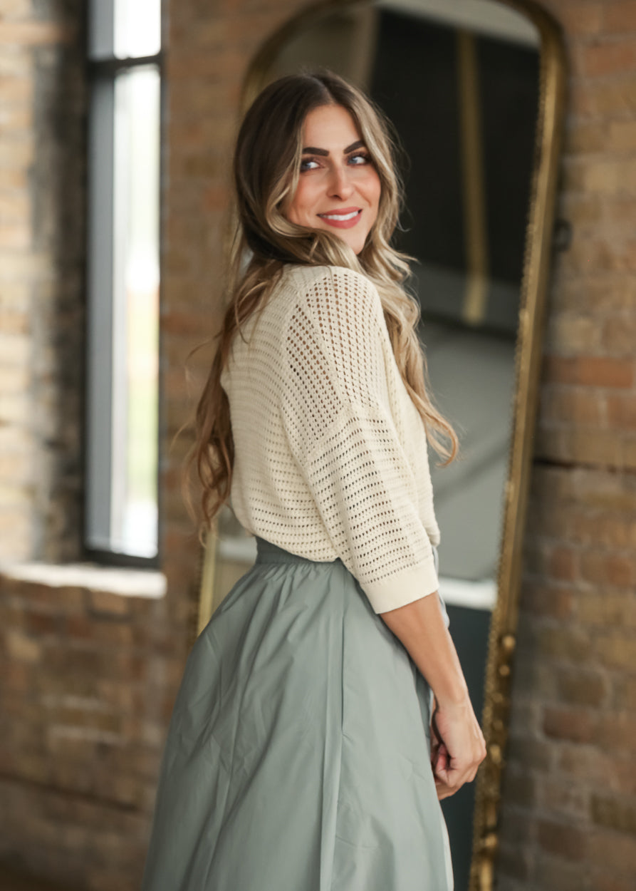 Cream short sleeve crochet cardigan with open knit texture and ribbed trim, styled with a sage maxi skirt.