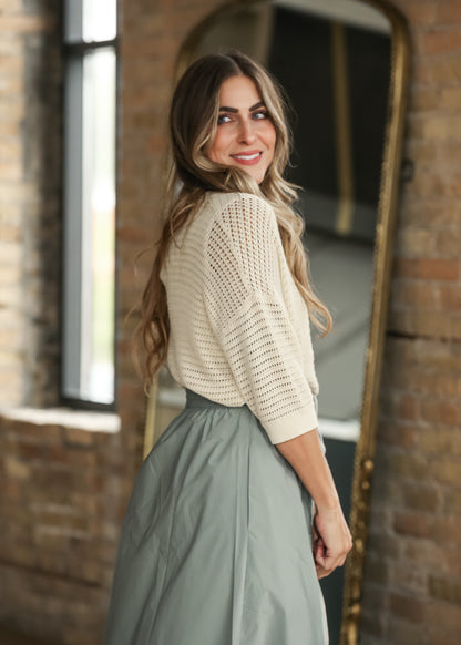 Cream short sleeve crochet cardigan with open knit texture and ribbed trim, styled with a sage maxi skirt.