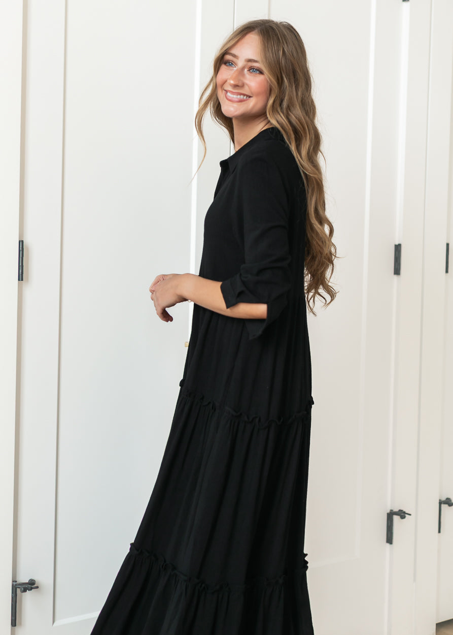 Black Elsie dress from the side showing the A-line silhouette and tiered midi skirt.