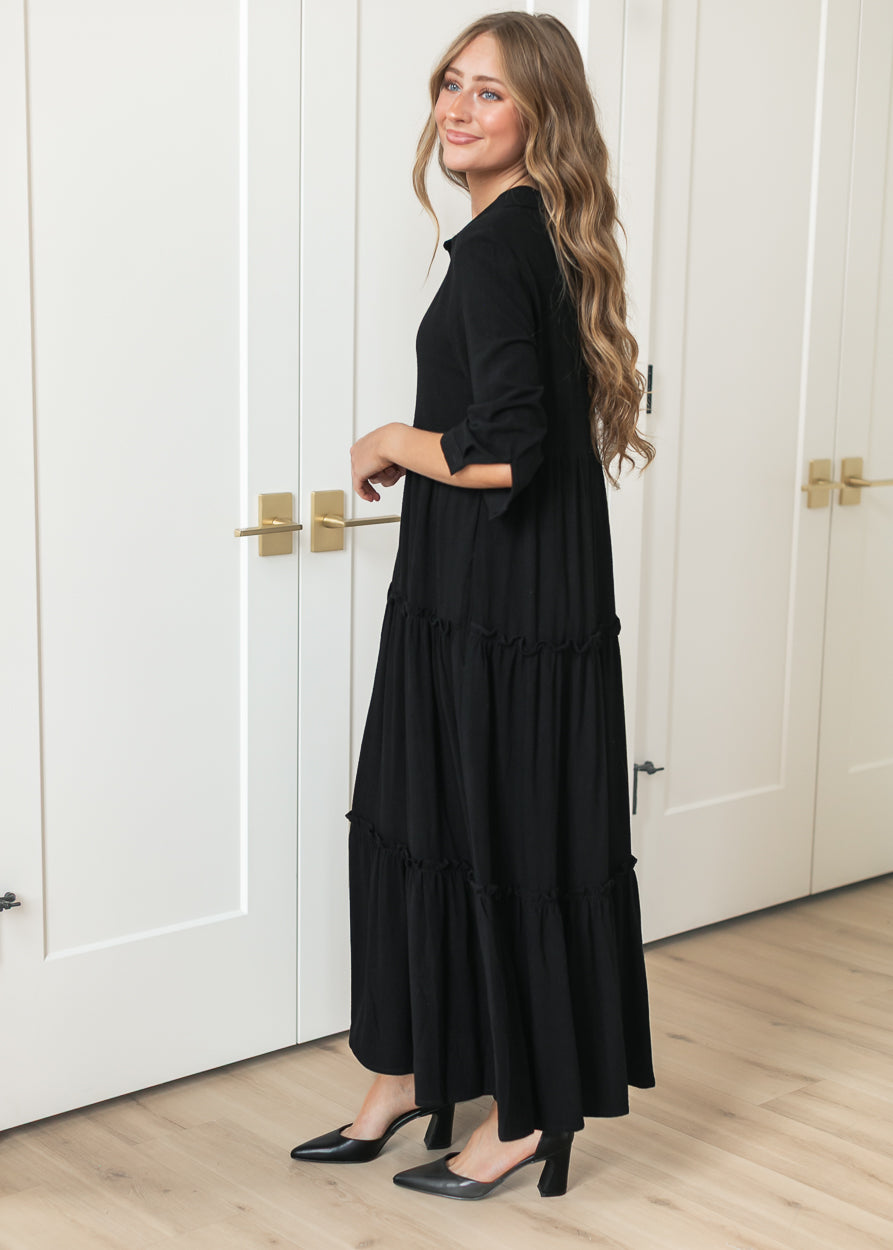 Side profile of black midi dress with half sleeves, button front, and tiered skirt.