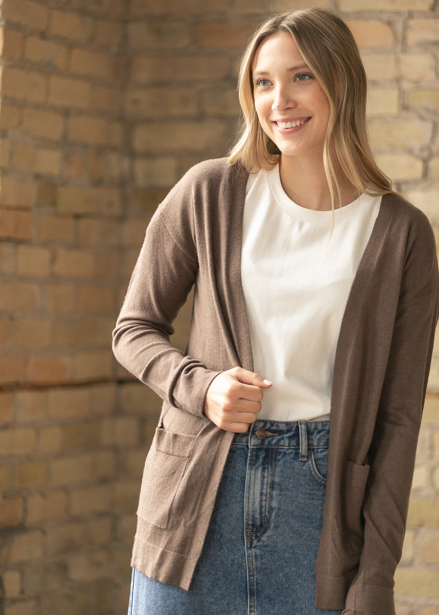 Close-up of the coffee cardigan front pocket and ribbed cuff against a cream top.