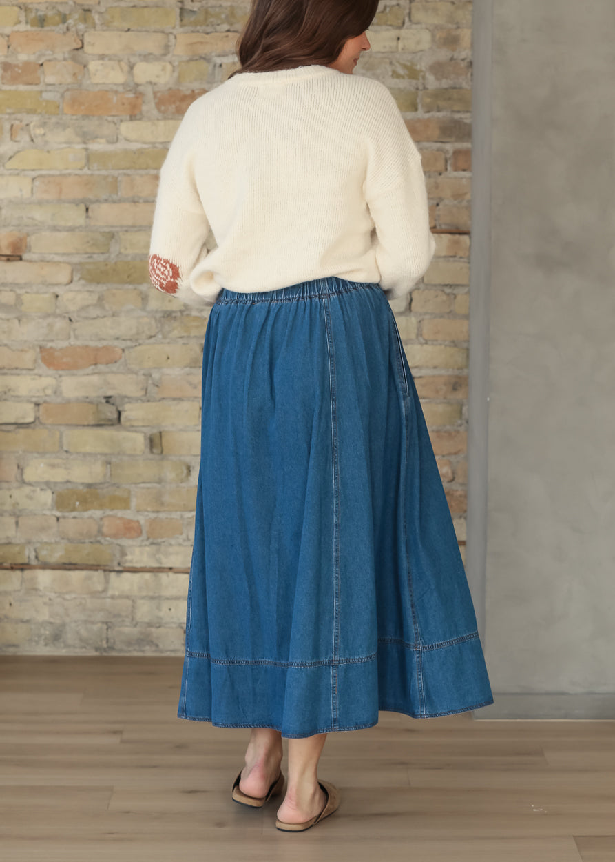 Full-length back view of cream floral sweater styled with a blue denim skirt