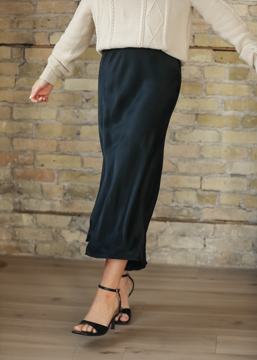 Model walking in a charcoal faux suede midi skirt with a cream cable knit sweater