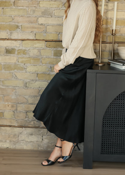 Model wearing a cream cable knit sweater with a charcoal faux suede midi skirt, side view