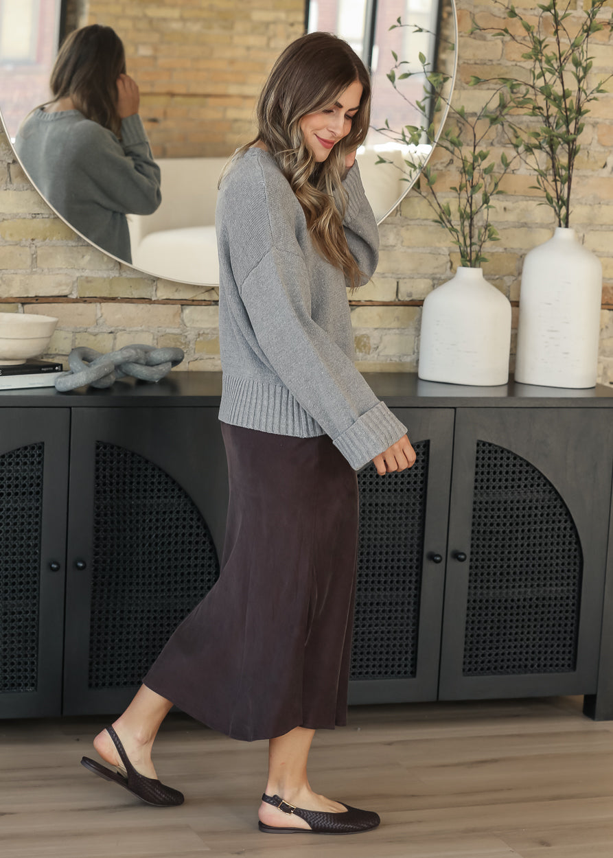 Full-length side view of dark chocolate faux suede midi skirt styled with a gray sweater and flats