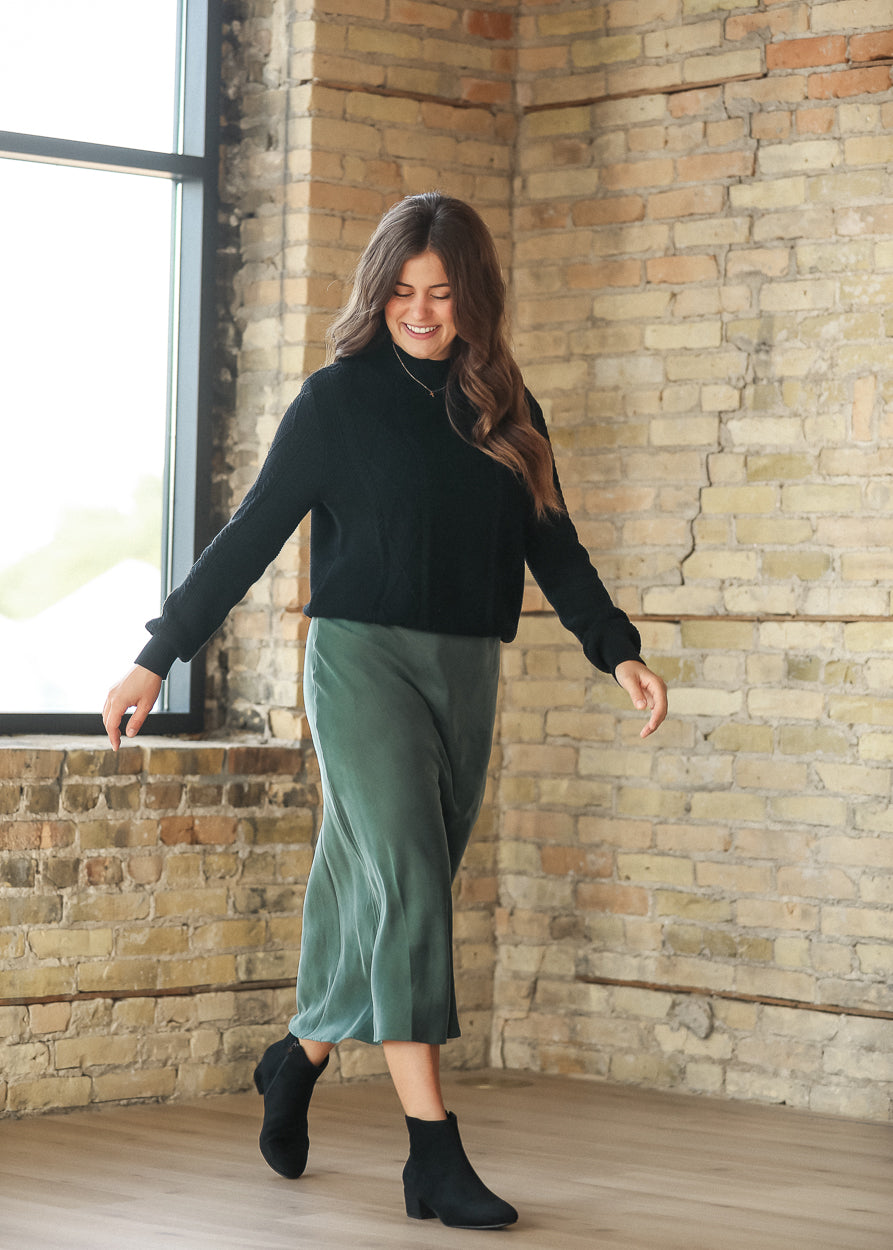Full-length movement view of emerald faux suede midi skirt styled with a black sweater