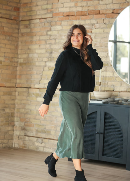 Model wearing an emerald faux suede midi skirt with a black sweater, walking view
