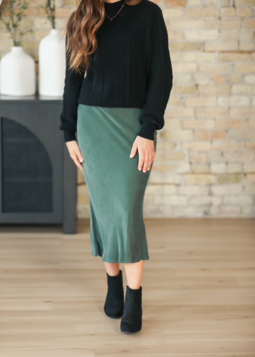 Full-length view of emerald faux suede midi skirt styled with a black sweater and boots