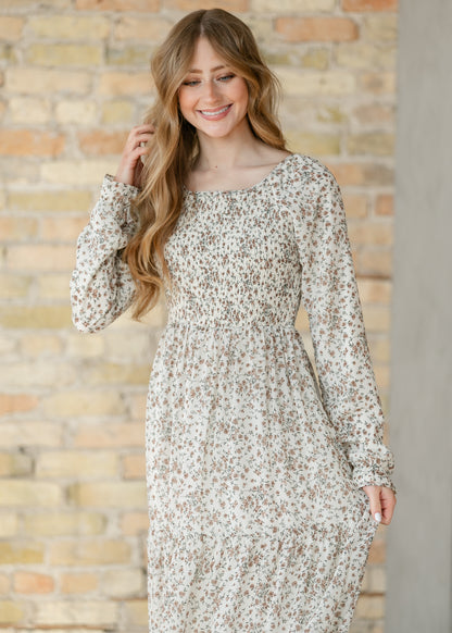 Woman wearing a floral dress against a brick wall.