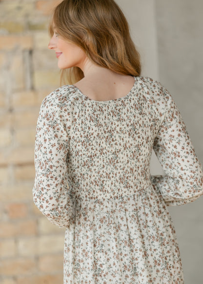 Back view of a woman wearing a floral dress standing against a brick wall.
