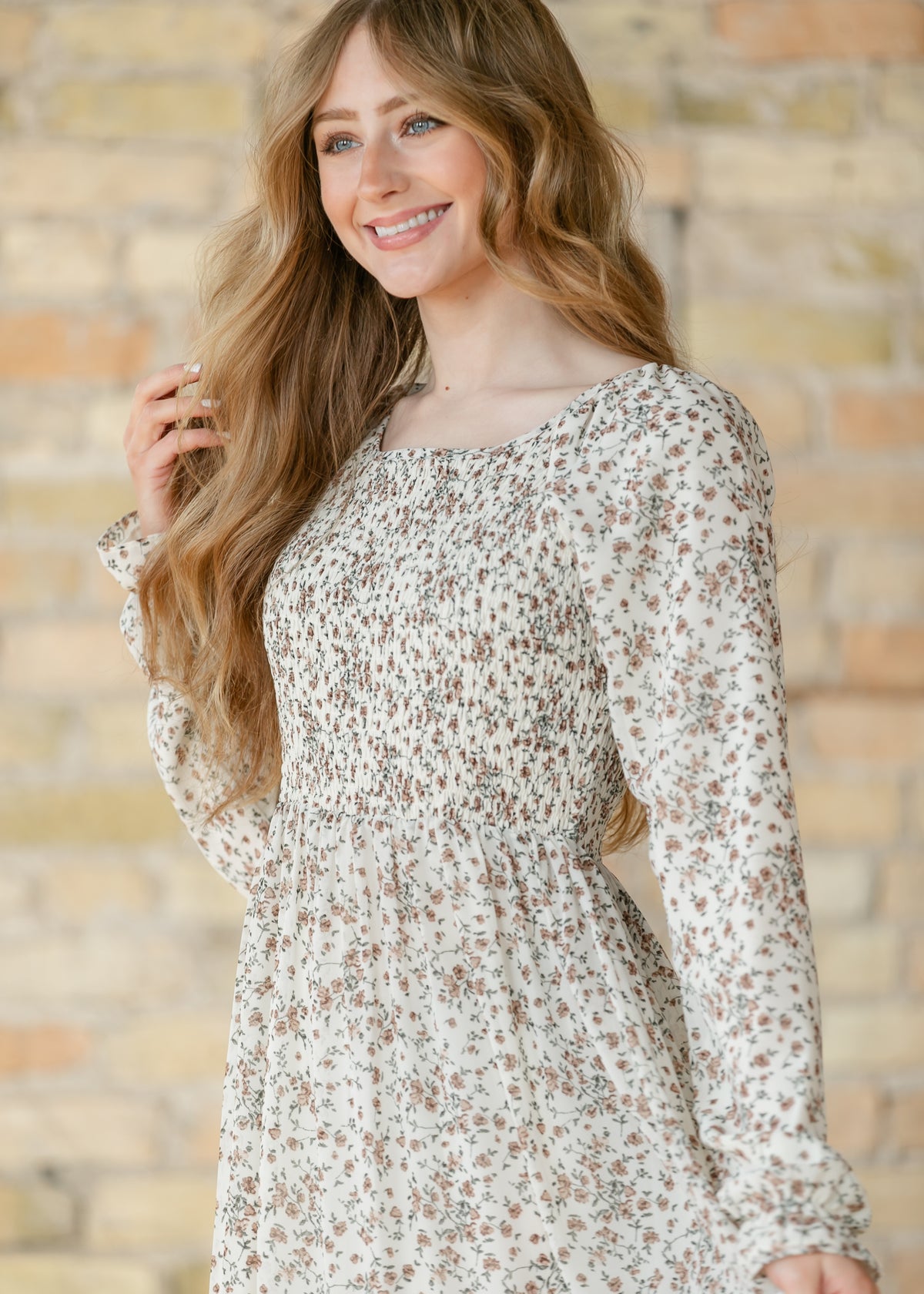 Close-up of a woman wearing a floral dress against a brick wall.