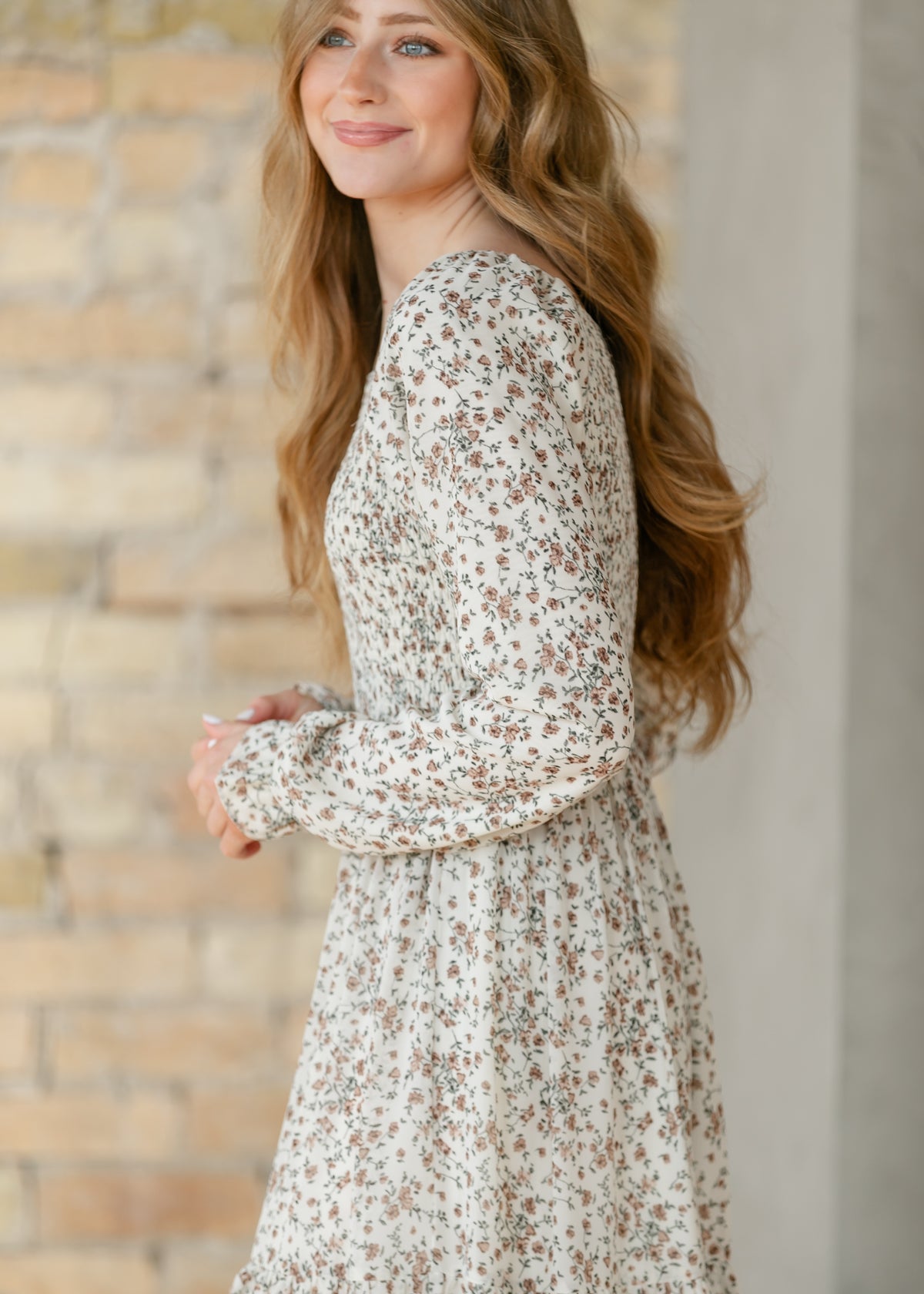 Side view of a woman wearing a floral dress standing against a brick wall.