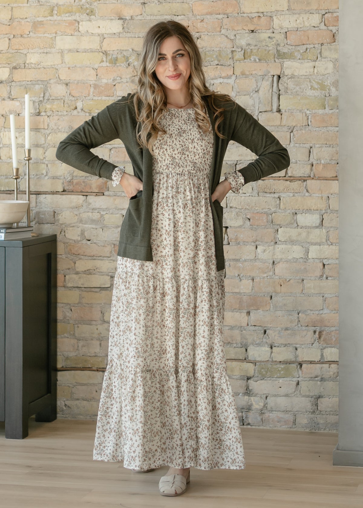 Woman wearing a floral dress and green cardigan against a stone wall.