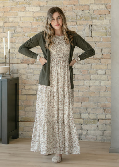 Woman wearing a floral dress and green cardigan against a stone wall.