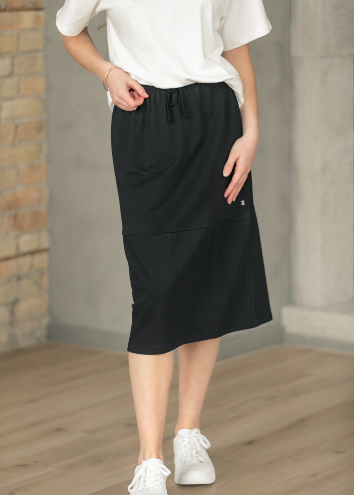 Black Gracie midi sweat skirt with pockets, styled with a tucked white tee and sneakers.