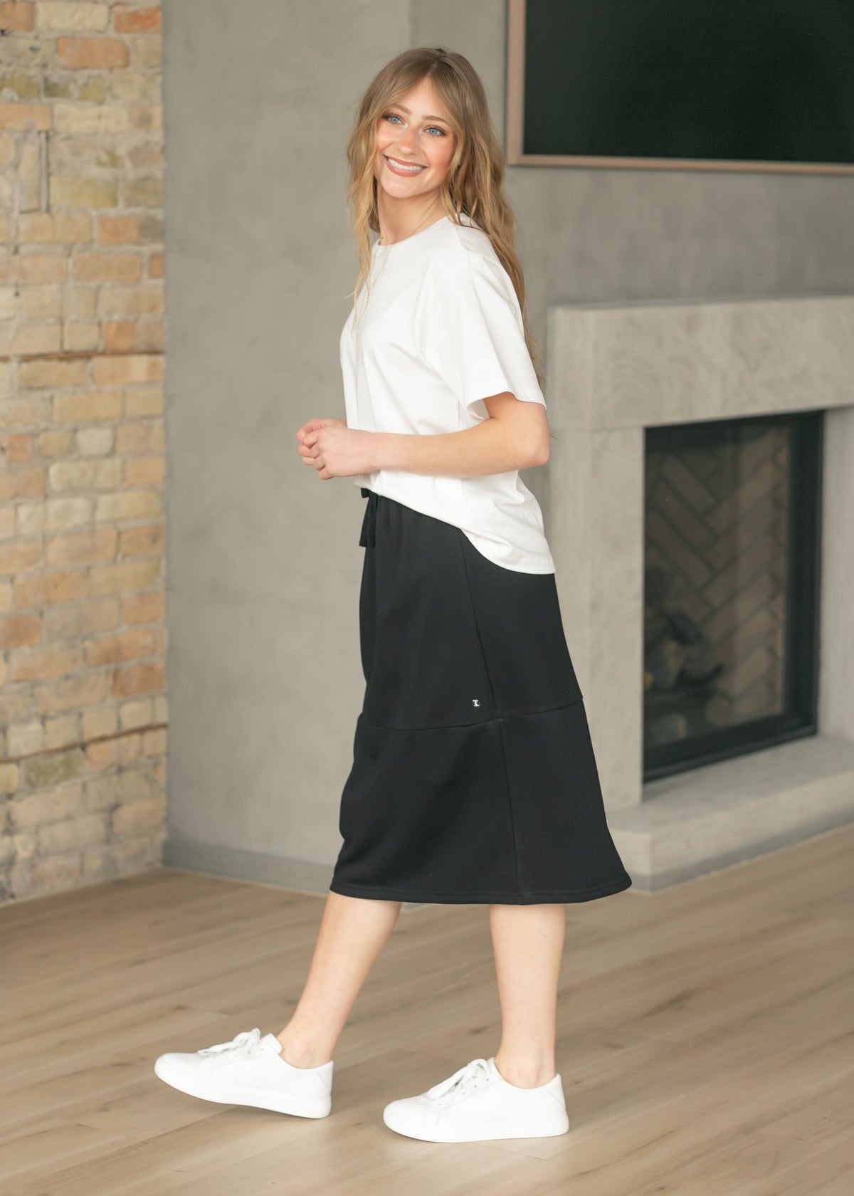 Gracie black midi skirt shown from the side with a relaxed fit, white tee, and sneakers.