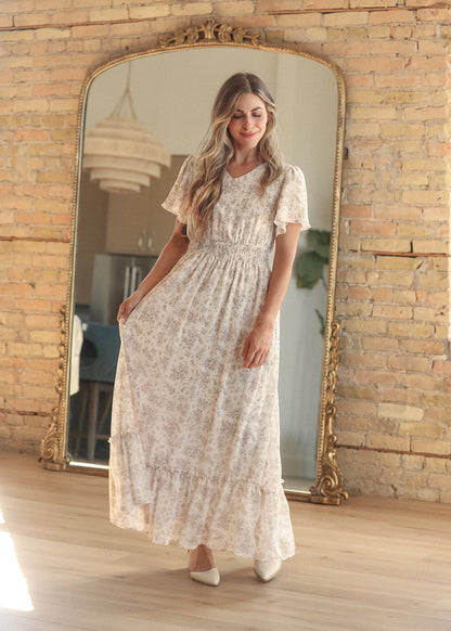 Cream floral maxi dress with a modest V-neck, flutter sleeves, and smocked waist detail.