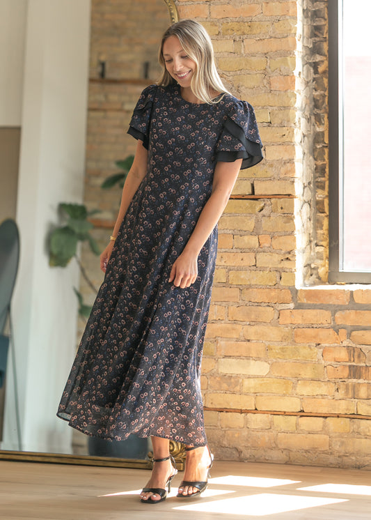 Navy floral maxi dress in a full-length pose with layered sleeves and softly moving skirt.