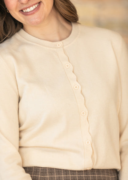 Close-up of ivory cardigan featuring scalloped trim and classic button front.