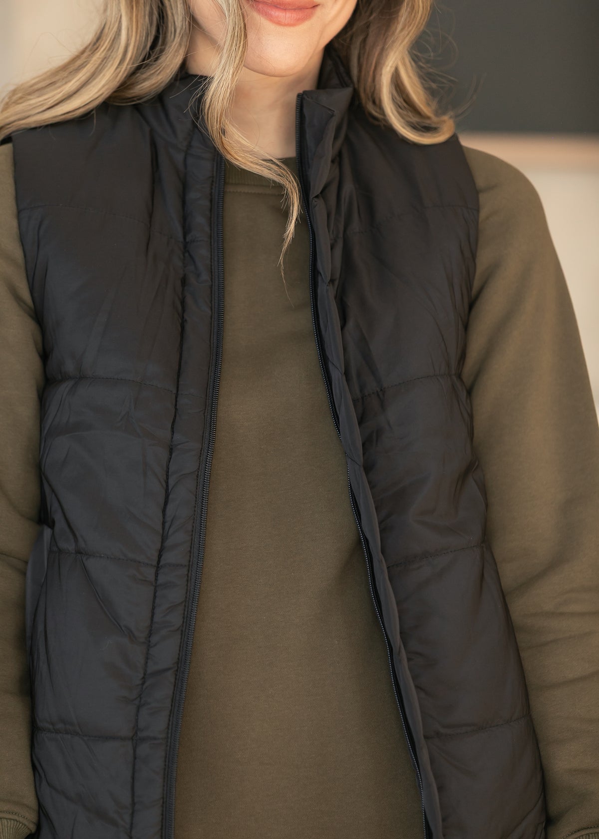 Detail of black quilted vest layered over an olive dress.