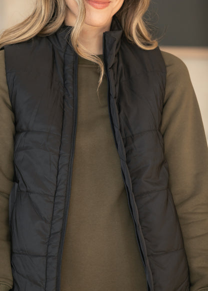 Detail of black quilted vest layered over an olive dress.