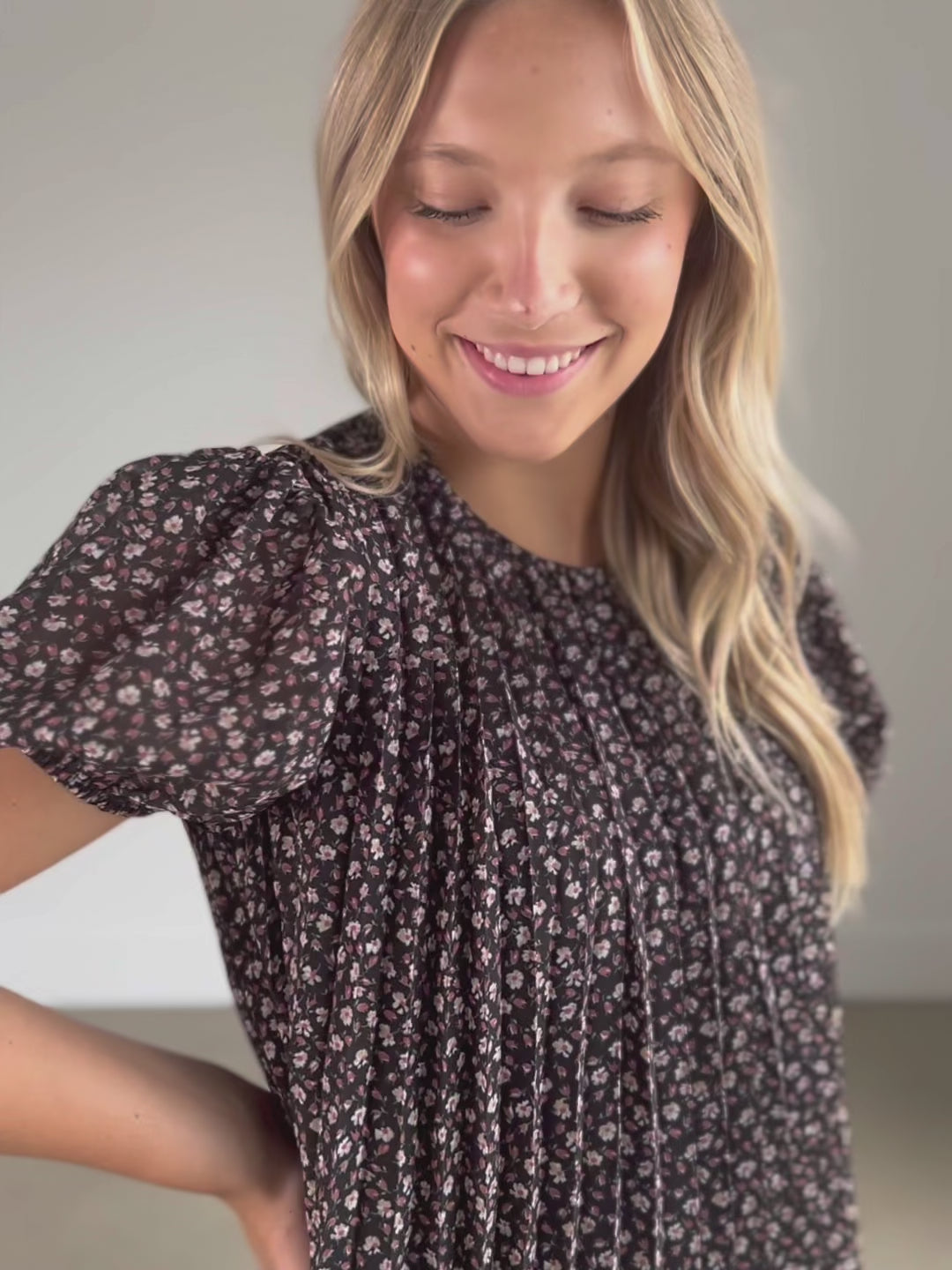 A black floral short sleeve top that is fully lined, with a round neckline, keyhole closure, and a pleated bodice.